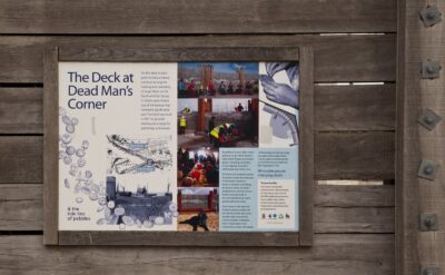 Information board on a timber wall explaining the site's history, the tide line of pebbles and the people who built it.