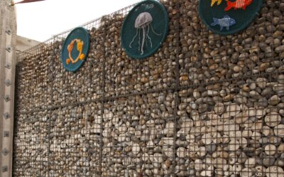 Wire cages packed with beach pebbles, with a band of patterned white ceramic pebbles set among them.