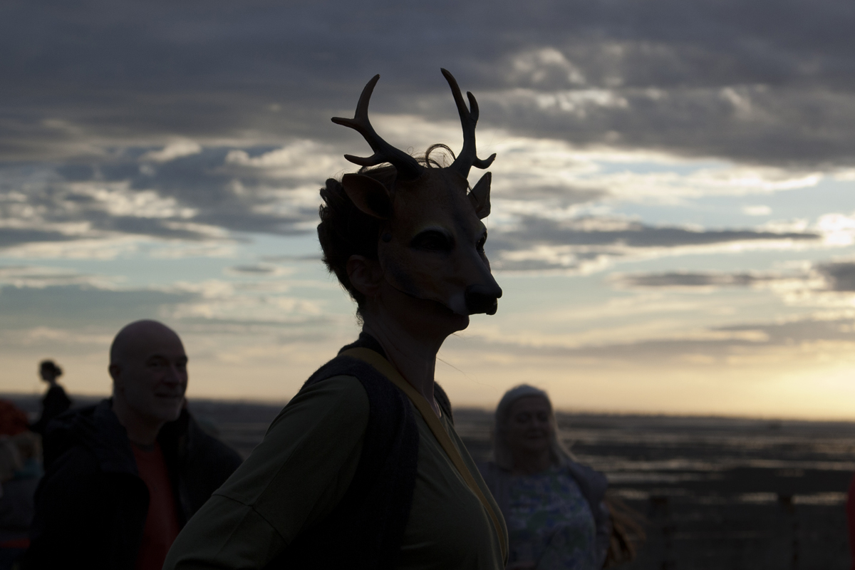 A person in a deer mask silhouetted against the evening sky over the Swale