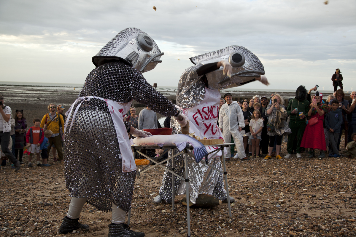 Two fish performers at a table as crumbs fly into the air and the crowd laughs