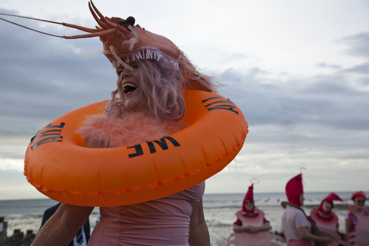 Sadie Hennessy laughing in a prawn headdress and orange swim ring on Whitstable beach