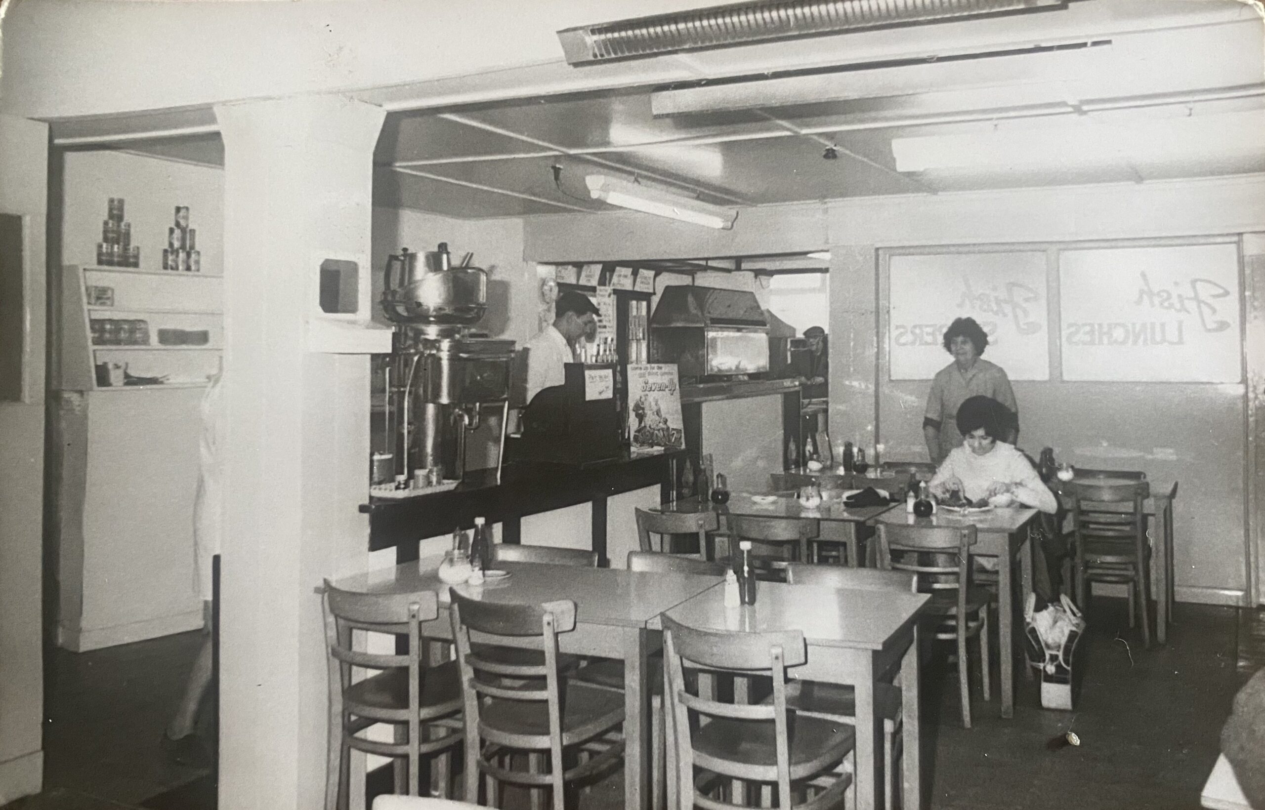 Interior of V C Jones fish and chip restaurant, Harbour Street, Whitstable, showing four unidentified people, formica tables and Fish Lunches painted on the window.