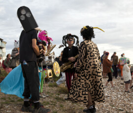 Masked musicians with saxophone, trombone and drum gather on Whitstable beach