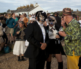Masked guests and onlookers mingle on Whitstable beach in front of white cottages