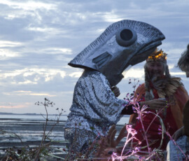 A performer in a sequinned fish head and Helene laughing at dusk on Whitstable beach