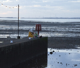 A figure in a white rabbit mask sits at the end of the jetty on Whitstable beach